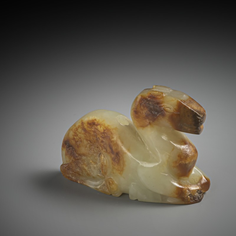 A Camel carved of green-caramel coloured jade on a wooden stand