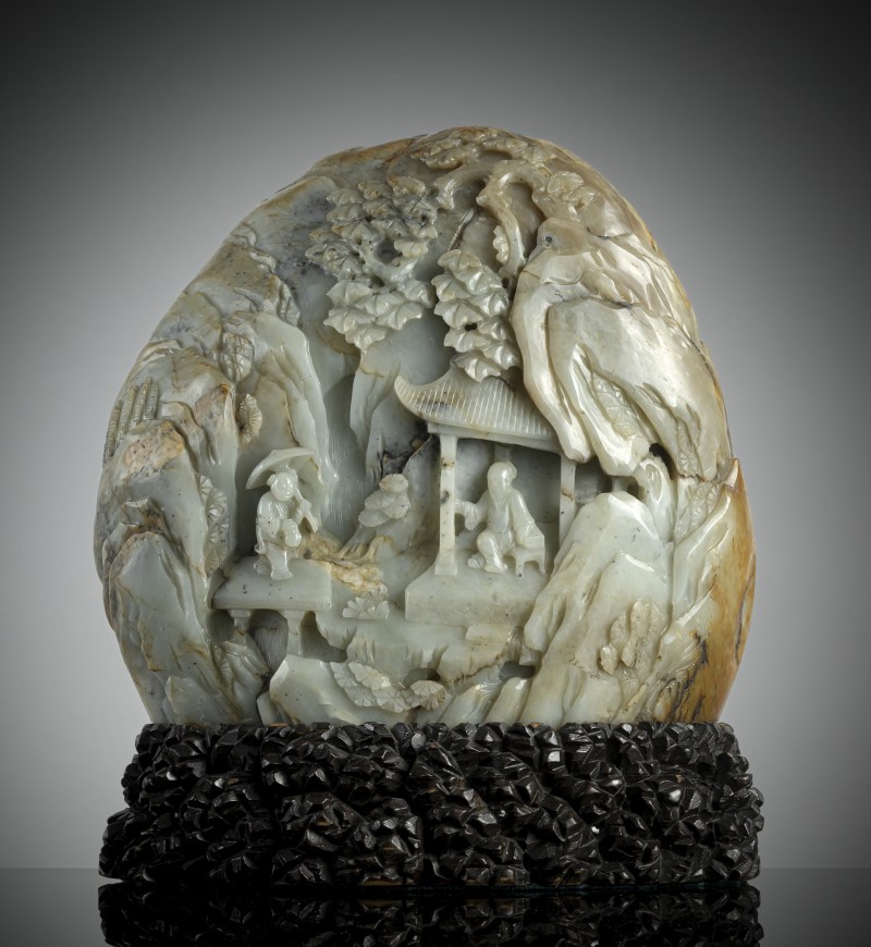 A large carved green jade boulder depicting scholars in a mountain landscape, mounted on a wooden stand