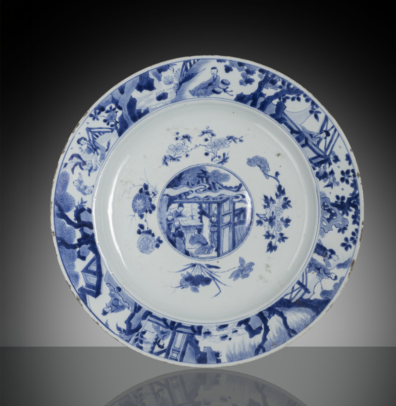 A large plate decorated in underglaze blue with figural scenes on the rim, in the raised nodus in the centre, lined with flowering branches