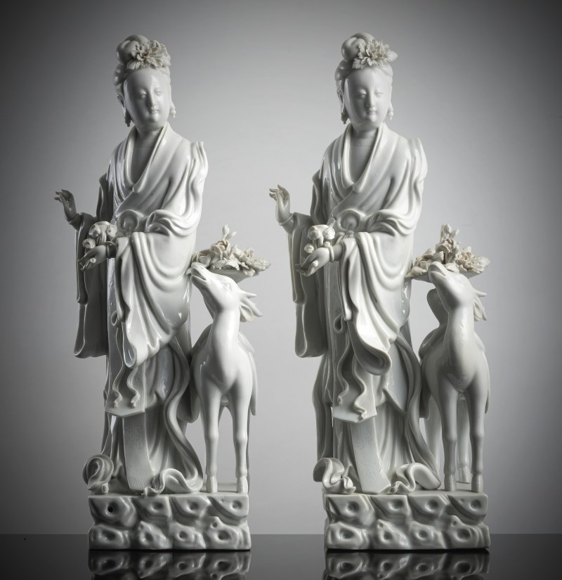 A pair of exquisite Dehua figurines depicting Magu with a deer, standing on a cloud-shaped pedestal with a basket of flowers