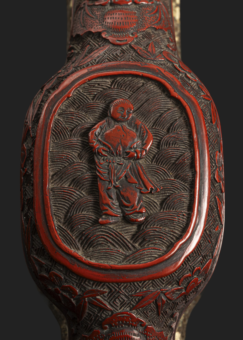 A fine carved cinnabar lacquer sceptre with a depiction of the Xiwangmu and boys next to bats and auspicious symbols on a stand
