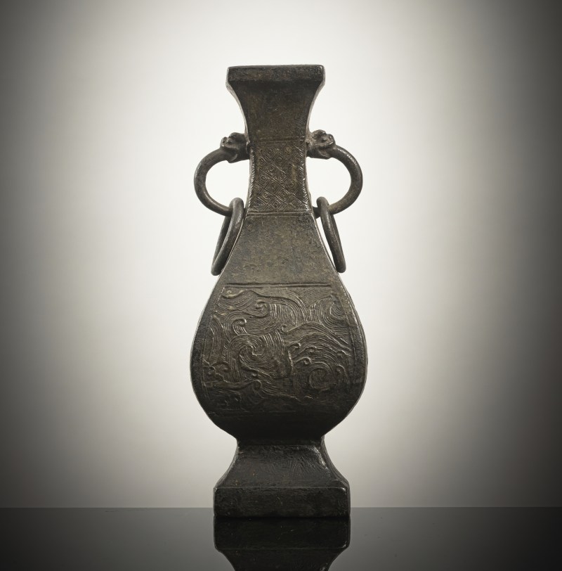 A four-sided bronze vase with wave decoration in relief and loose ring handles