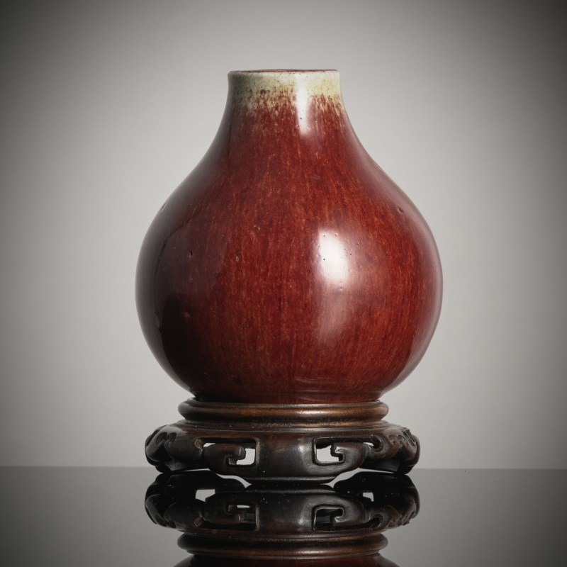 A small oxblood-glazed porcelain vase on wood stand