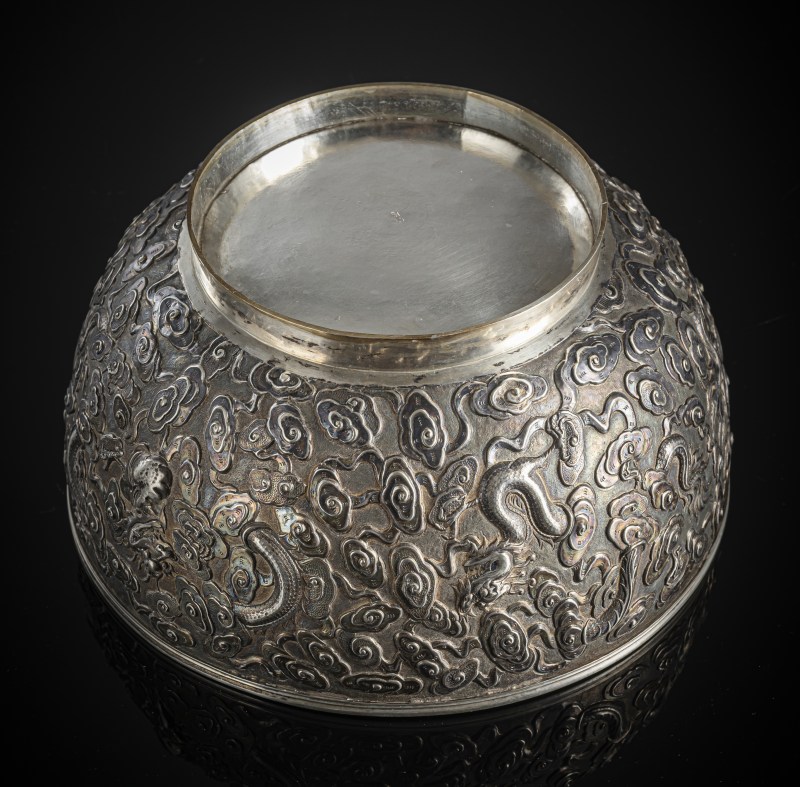 A large silver bowl with embossed decoration of four dragons between clouds around an inscription cartouche