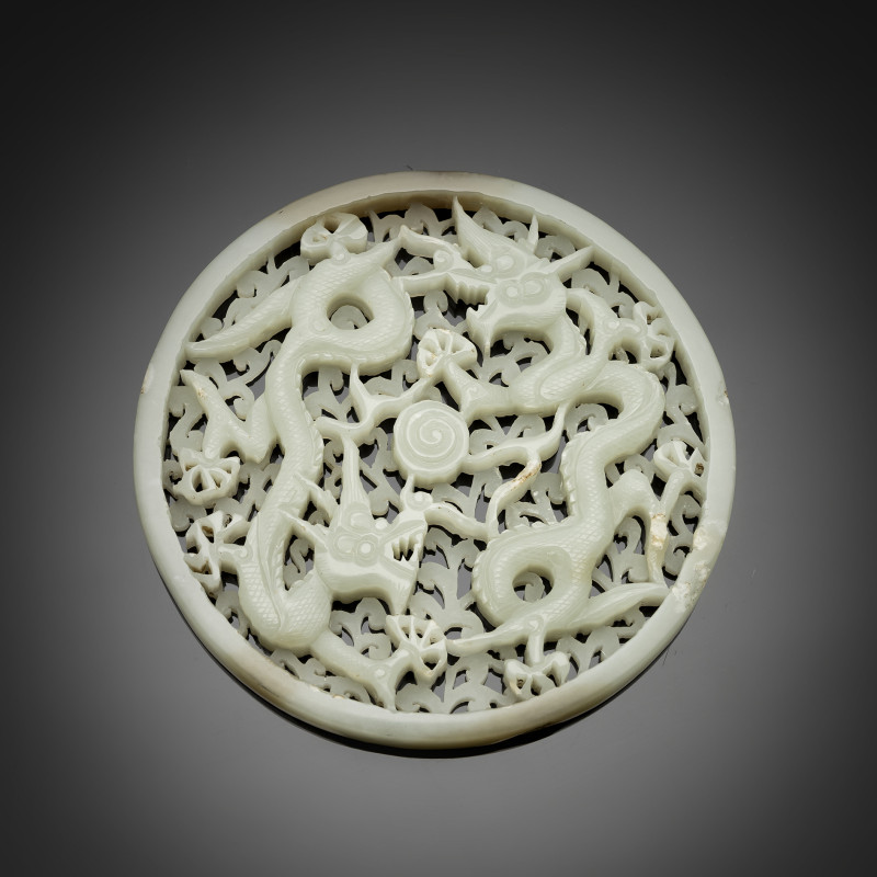 A circular light green jade plaque with a dragon in an opening