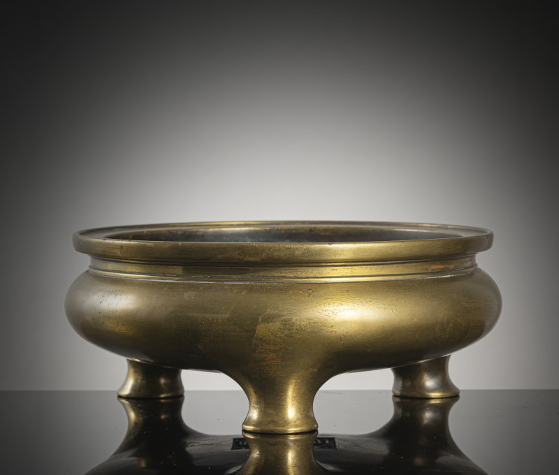 A flat heavy cast incense burner made of gold-coloured bronze on three short feet
