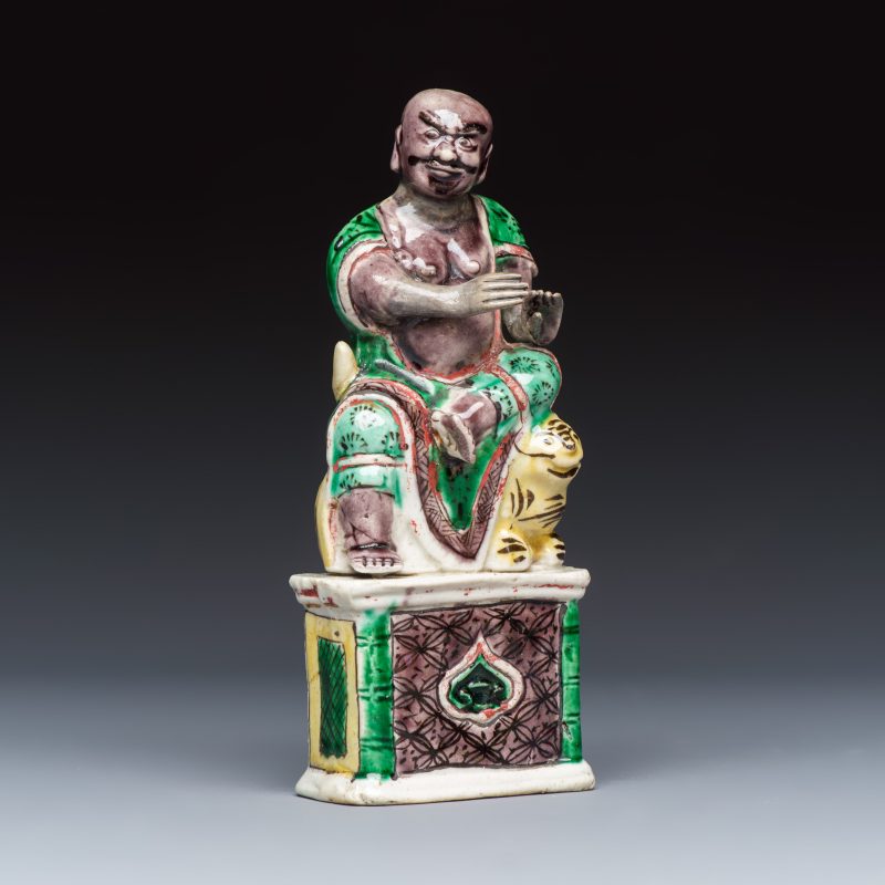 A Chinese famille verte sancai biscuit model of a seated Luohan on a tiger