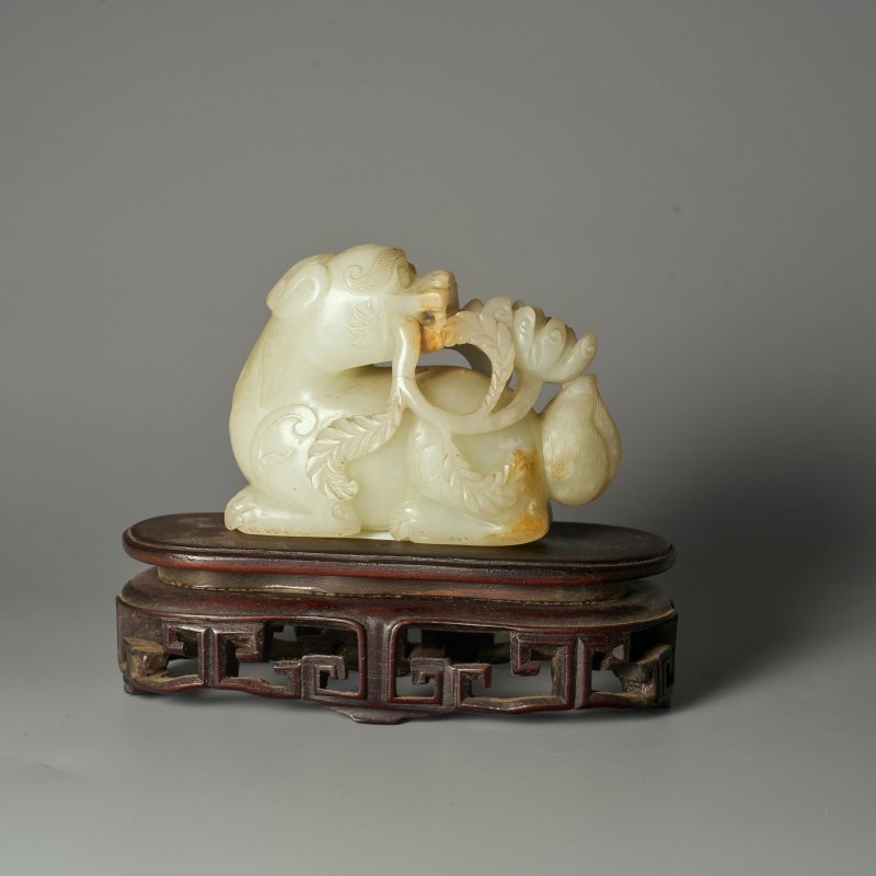 清 青白玉瑞獸銜花擺件 及座 | A GREENISH WHITE JADE 'DOG' CARVING WITH RUSSET INCLUSION